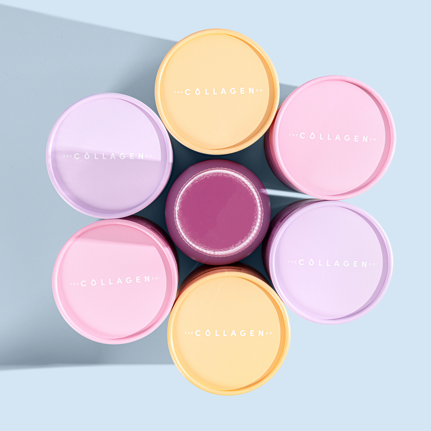 Colorful round containers of collagen supplements arranged in a flower shape on a light blue background.