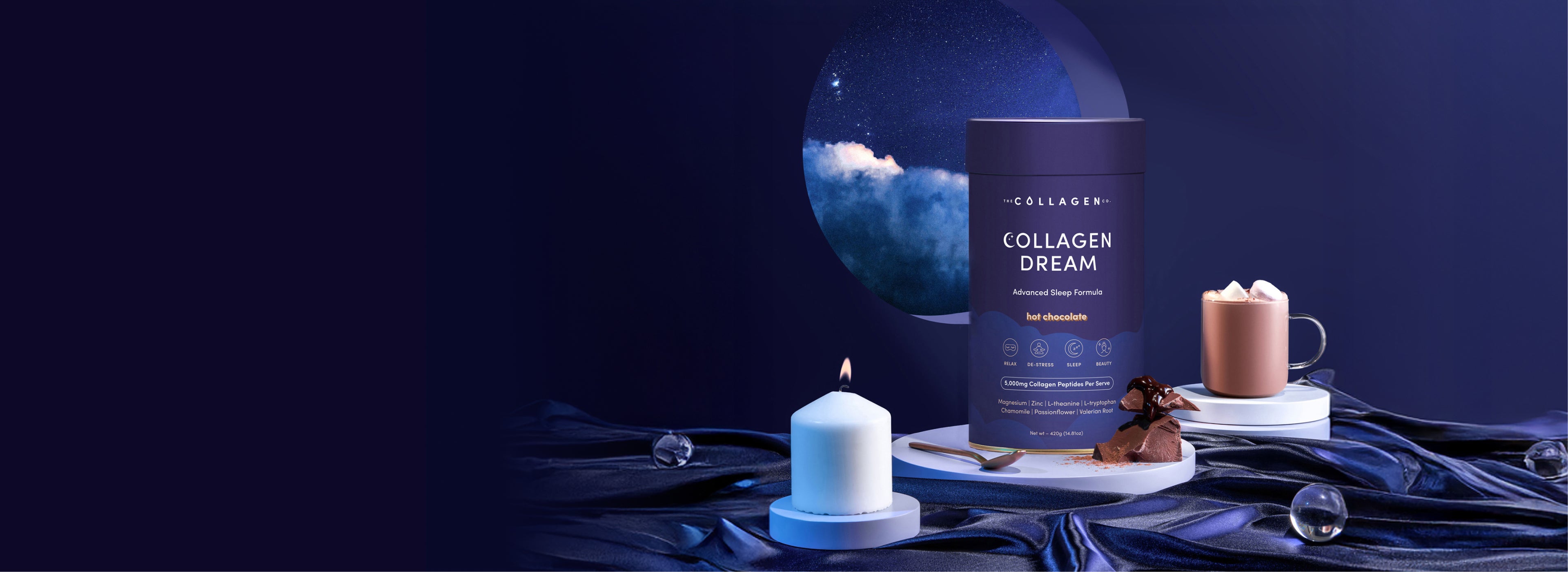 A blue container labeled “Collagen Dream” sits on a silky blue cloth beside a lit candle, a mug of hot chocolate with whipped cream, chocolates, glass orbs, and a circular window showing a night sky with clouds and stars.