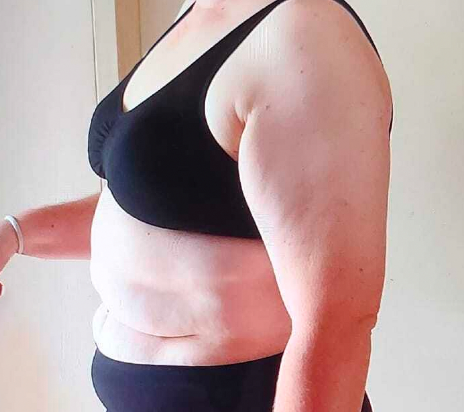 Side profile of a person in a black sports bra and shorts, showcasing midsection before using supplements for weight loss or beauty enhancement.