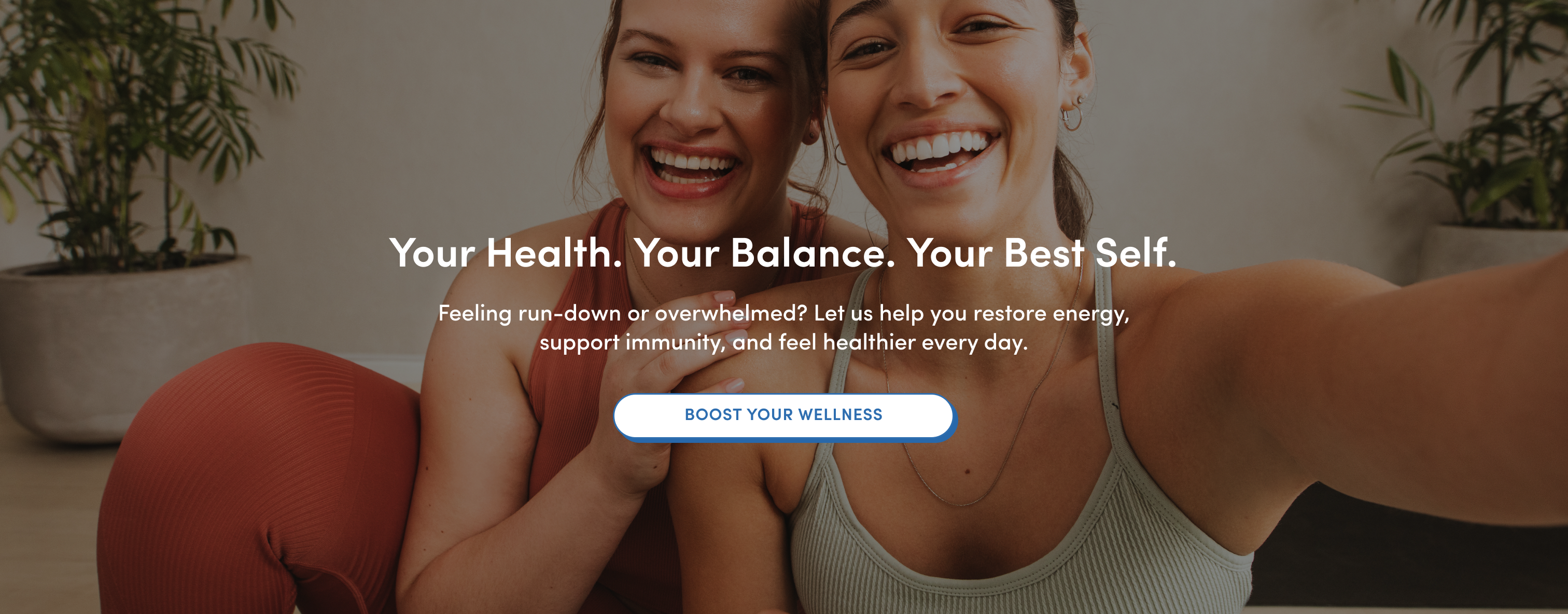 Two smiling women in workout clothes sit close together indoors, appearing happy and energetic. Text over the image promotes health, balance, and wellness, with a button labeled “Boost Your Wellness” below the description.