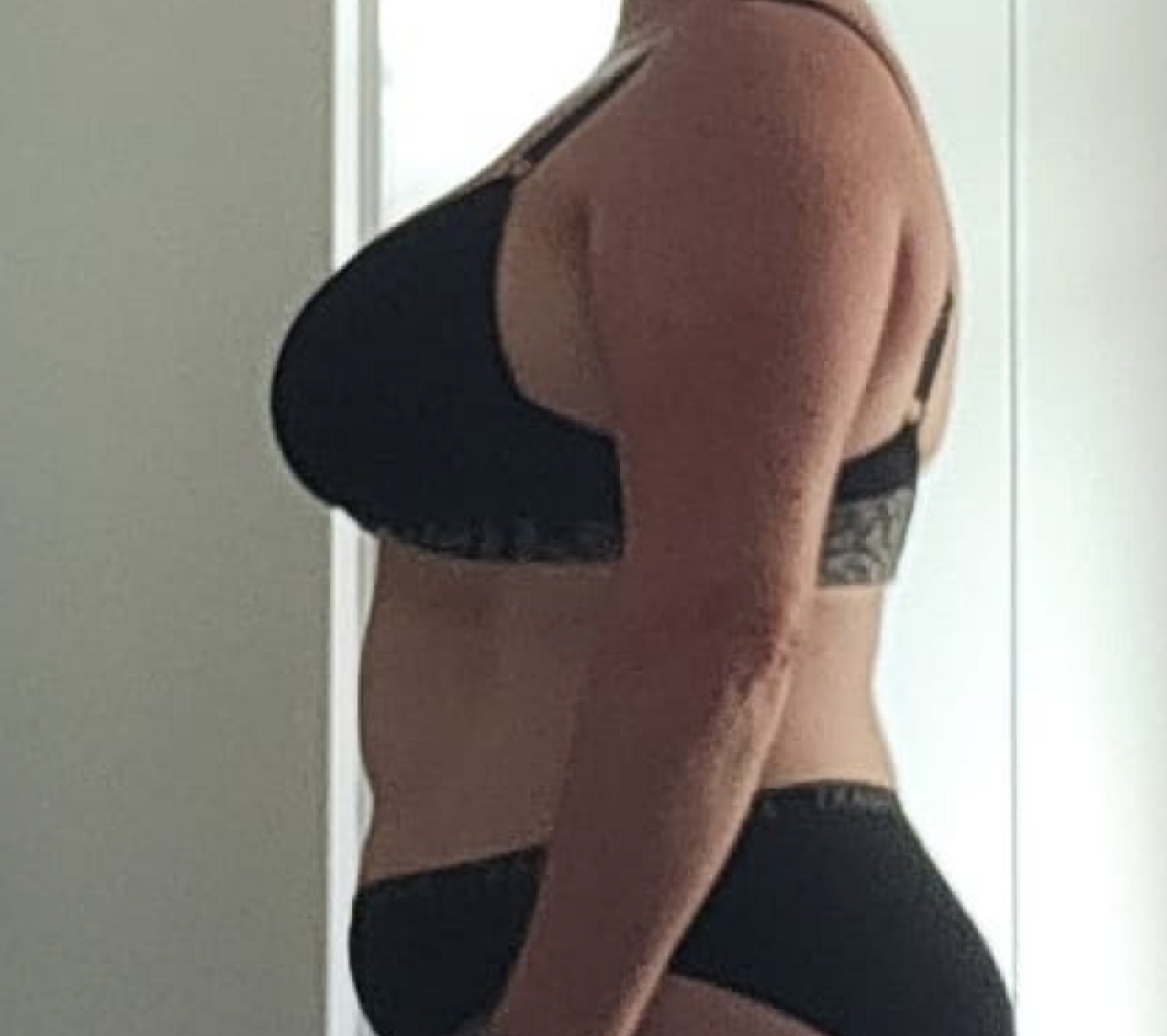 Person in black underwear standing sideways, showcasing body profile. Bright, neutral background.