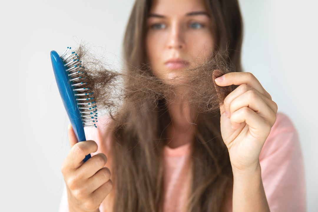 Woman looking at hair loss on a blue brush, highlighting beauty concerns.