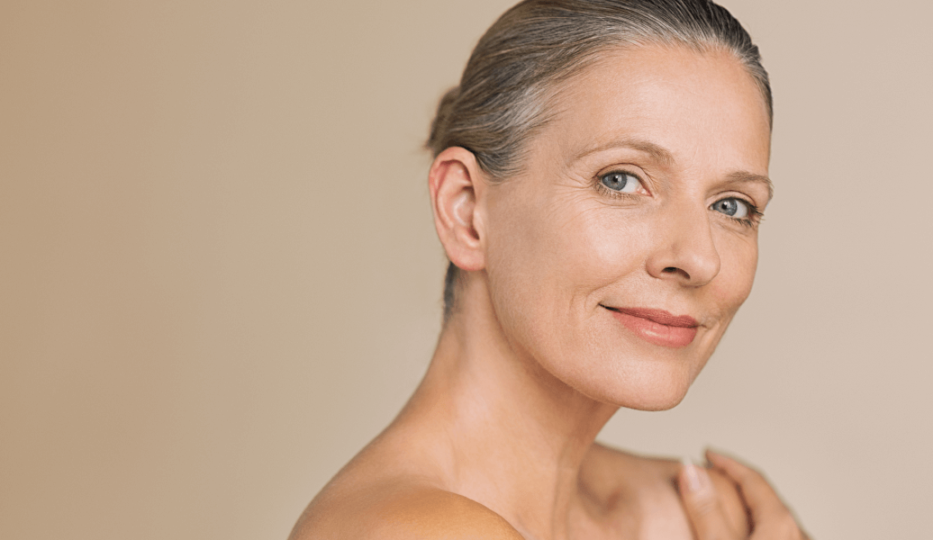 Smiling mature woman with smooth skin and natural makeup, showcasing beauty and skincare. Warm background enhances radiant complexion.
