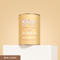 A tan canister of Glow Shakes iced coffee flavour collagen meal replacement displayed on a white block against a beige background. The front of the packaging emphasizes benefits like metabolism boost, skin glow, and energy support.