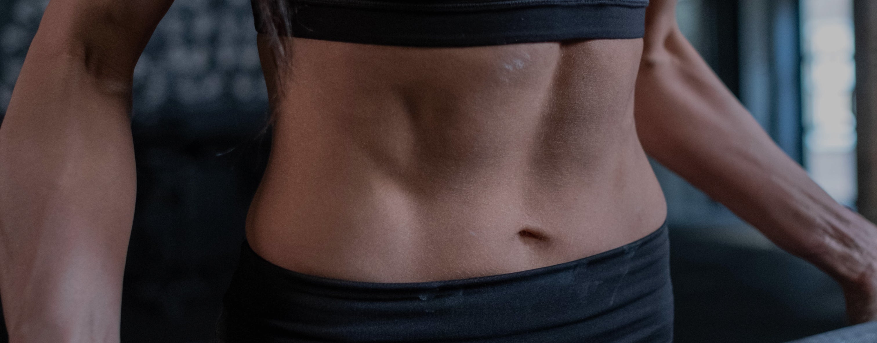 Fit woman's toned midsection in black athletic wear, highlighting muscle definition and strength. Fitness and health-focused imagery.