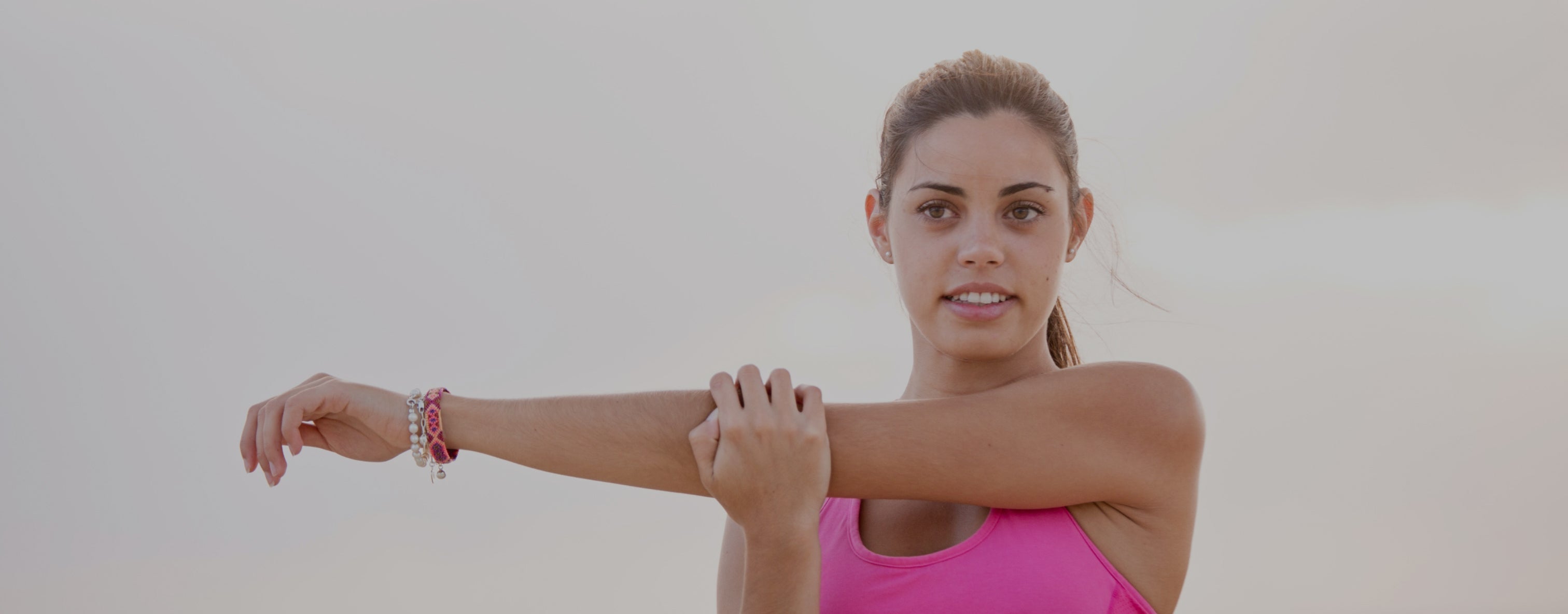 Woman in pink tank top stretching her arm outdoors, promoting fitness, health, and beauty supplements.