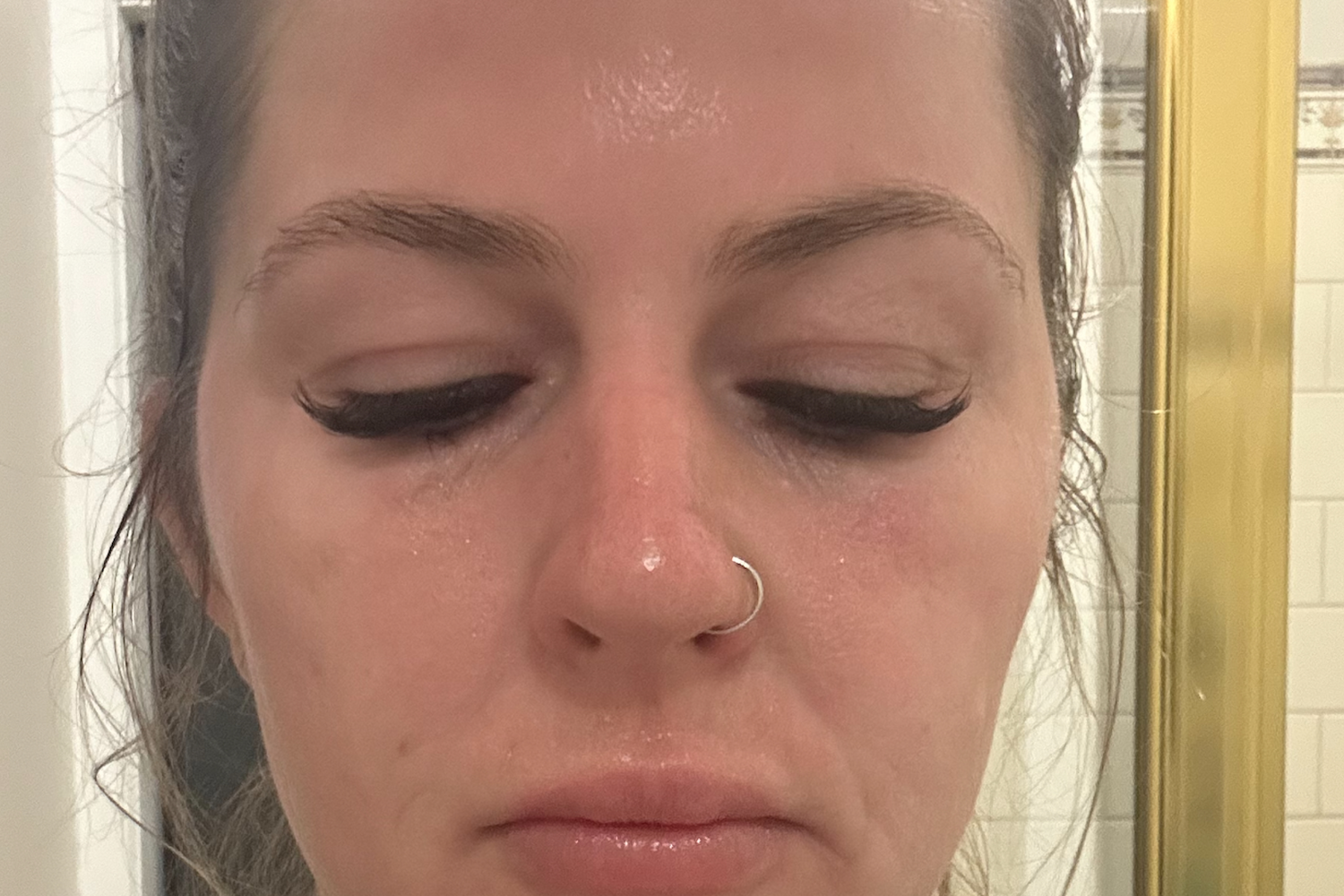 Close-up of a woman's face with long eyelashes and a nose ring, appearing to have a dewy complexion, suggesting skincare or beauty routine.