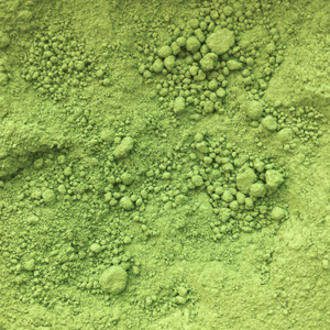 Close-up of green powder texture, resembling matcha or a supplement, with fine and coarse clumps scattered across the surface.