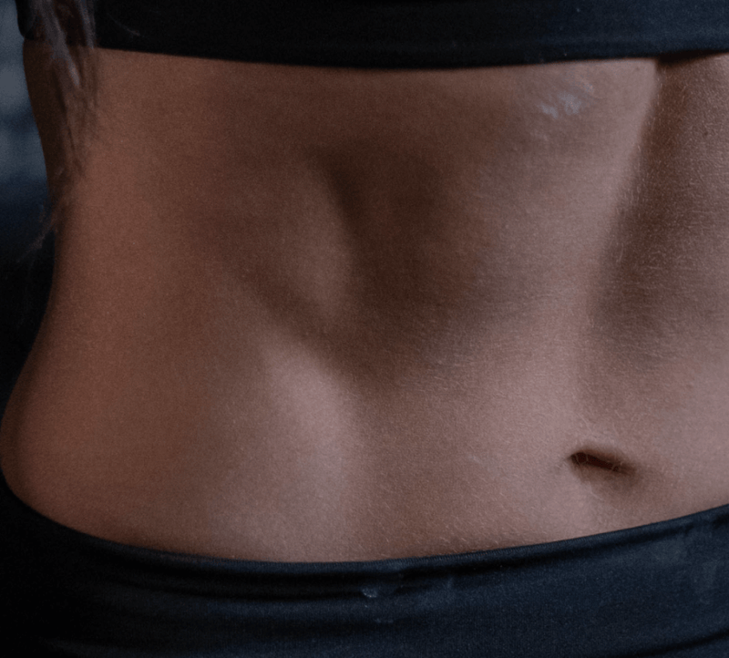 Close-up of a toned, smooth abdomen with defined muscles, wearing a black waistband. Perfect for beauty and fitness-focused content.