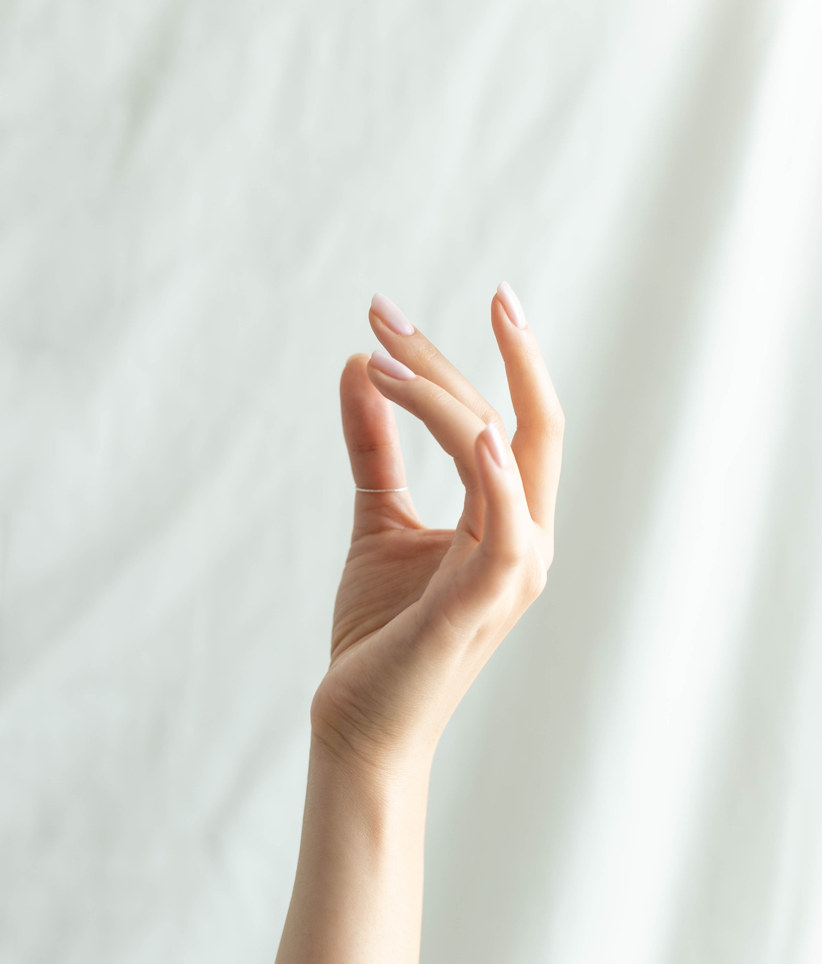 A graceful hand with manicured nails posed elegantly against a soft, light background, highlighting beauty and skincare themes.
