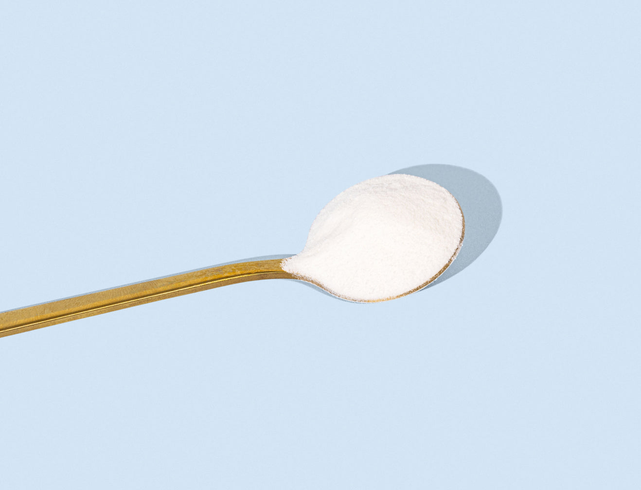 Spoon with white collagen powder against a light blue background, highlighting beauty supplement.