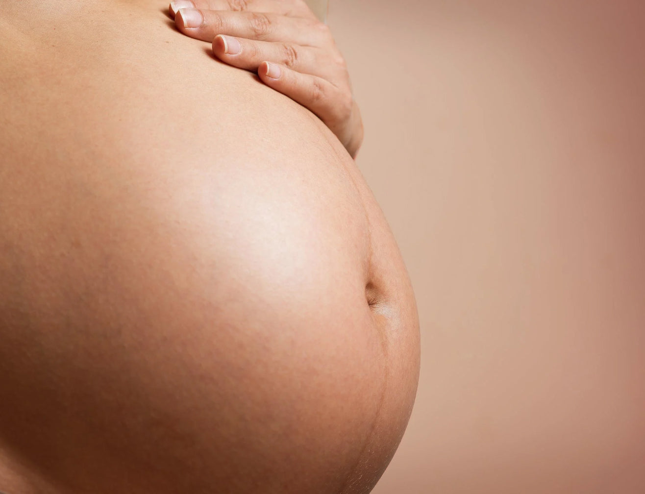 Close-up of a pregnant belly with a hand gently resting on top, highlighting skin texture and maternal beauty.