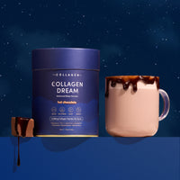 A container of The Collagen Co. Collagen Dream Advanced Sleep Formula Hot Chocolate - 210g sits by a pink mug with chocolate drips and a piece of chocolate, set against a dark starry night—perfect for restful, skin-supporting indulgence.