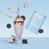 A glass of The Collagen Co. Cookies & Cream Collagen Meal Replacement (784g) is topped with whipped cream and caramel, surrounded by Oreo cookies, cookie dough, and a Glow Shakes canister—made with hydrolyzed collagen peptides.