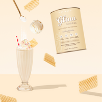 A glass of The Collagen Co. Vanilla Milkshake Collagen Meal Replacement sits with a canister, waffle cookies, and ice cream on a beige background—an ideal choice for weight management.