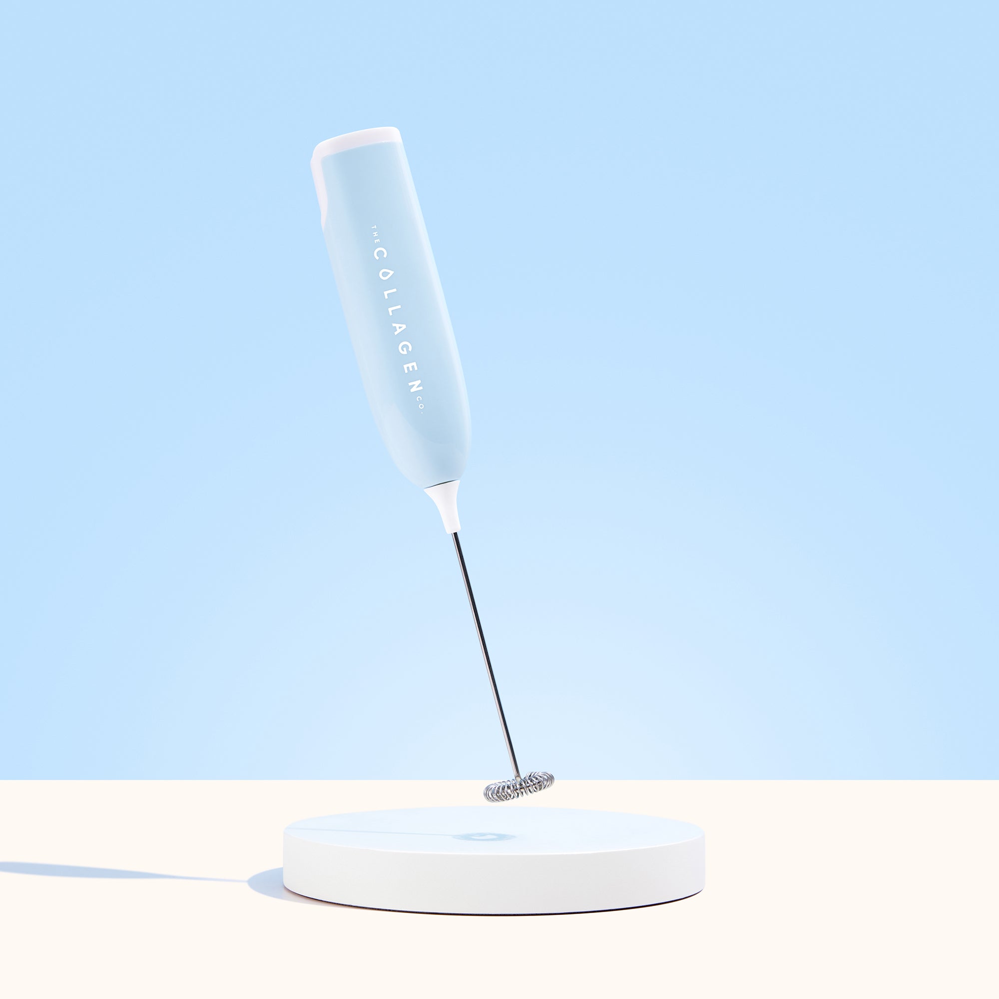 A light blue Collagen Mixer by The Collagen Co USA stands upright on a round white base against a matching light blue background.