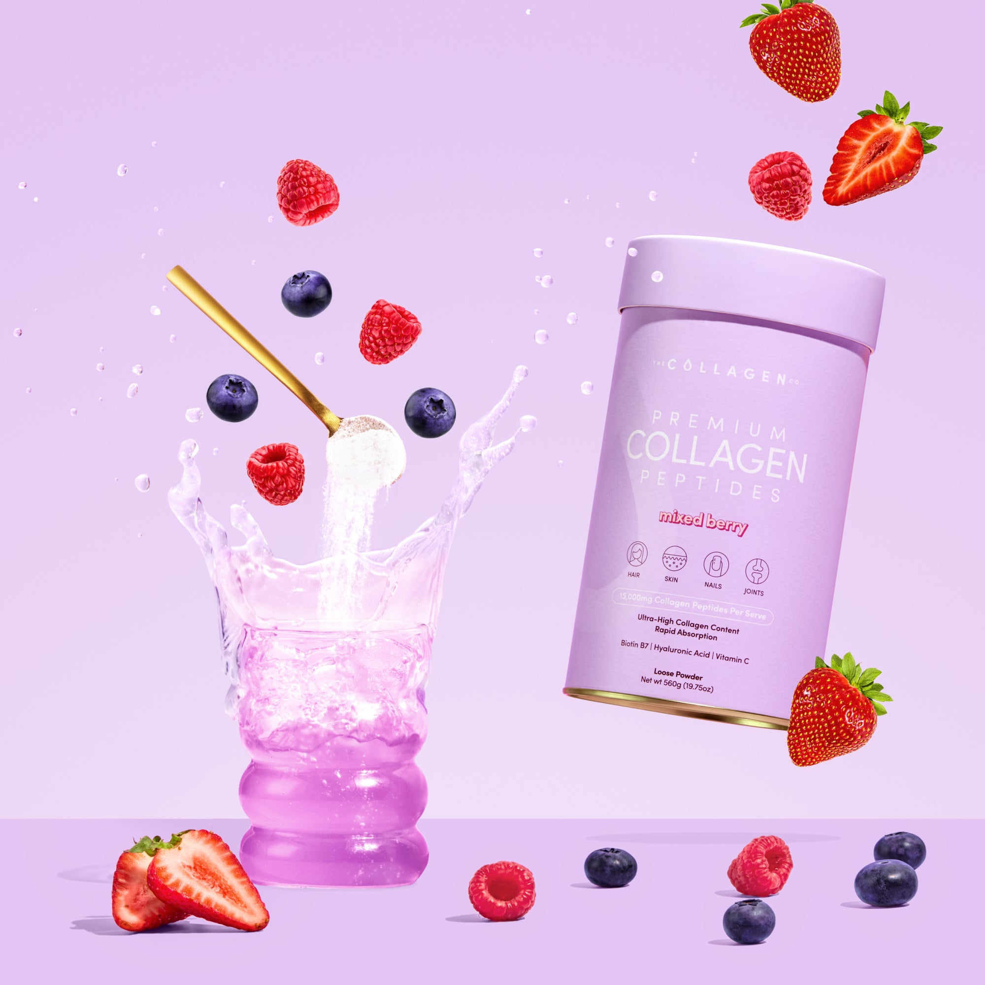 A pink canister of The Collagen Co. Mixed Berry Collagen Powder (560g) floats beside a glass of pink liquid with a straw, as water splashes and berries hover against a pastel purple background, highlighting hydrolysed bovine collagen.