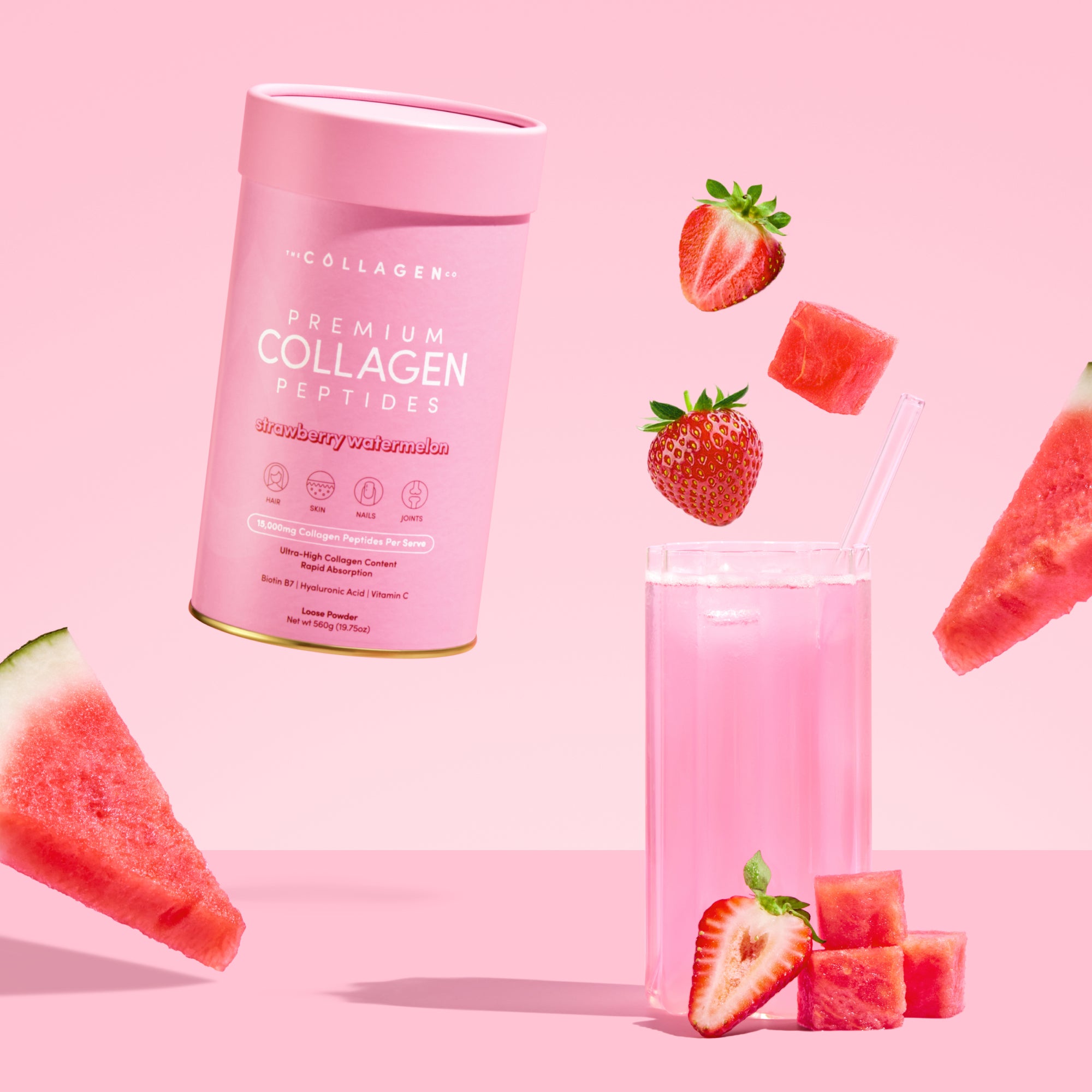 The Strawberry Watermelon Collagen Powder (560g) from thecollagen.co is displayed in a pink canister alongside a glass of pink drink, strawberries, watermelon slices, and cubes on a pink background with some fruit pieces floating above.