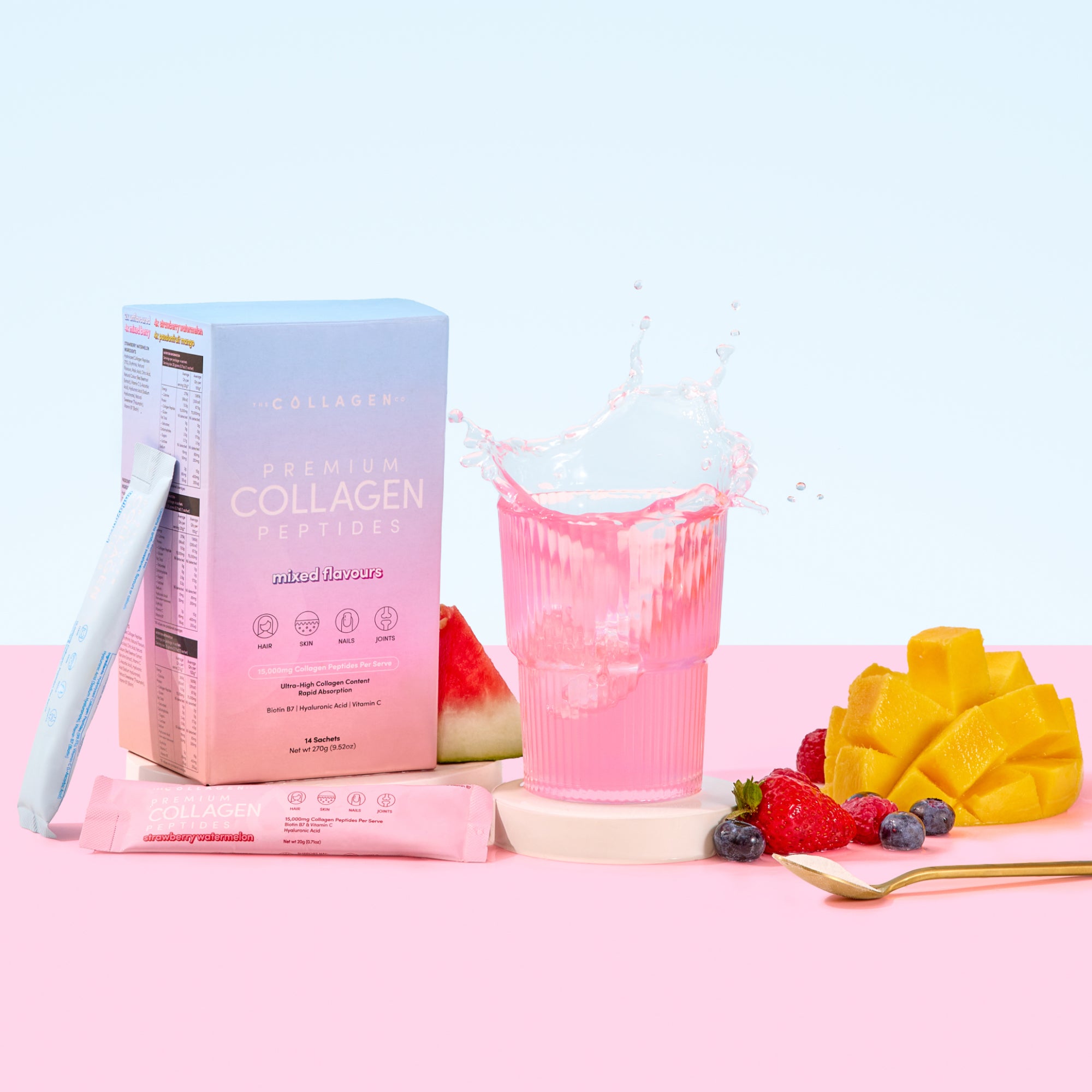 A box of thecollagen.co Mixed Flavors Collagen Sachets (270g), a vibrant pink anti-ageing drink, fresh watermelon, diced mango, berries, and a single sachet are artfully arranged on a pastel pink and blue background.