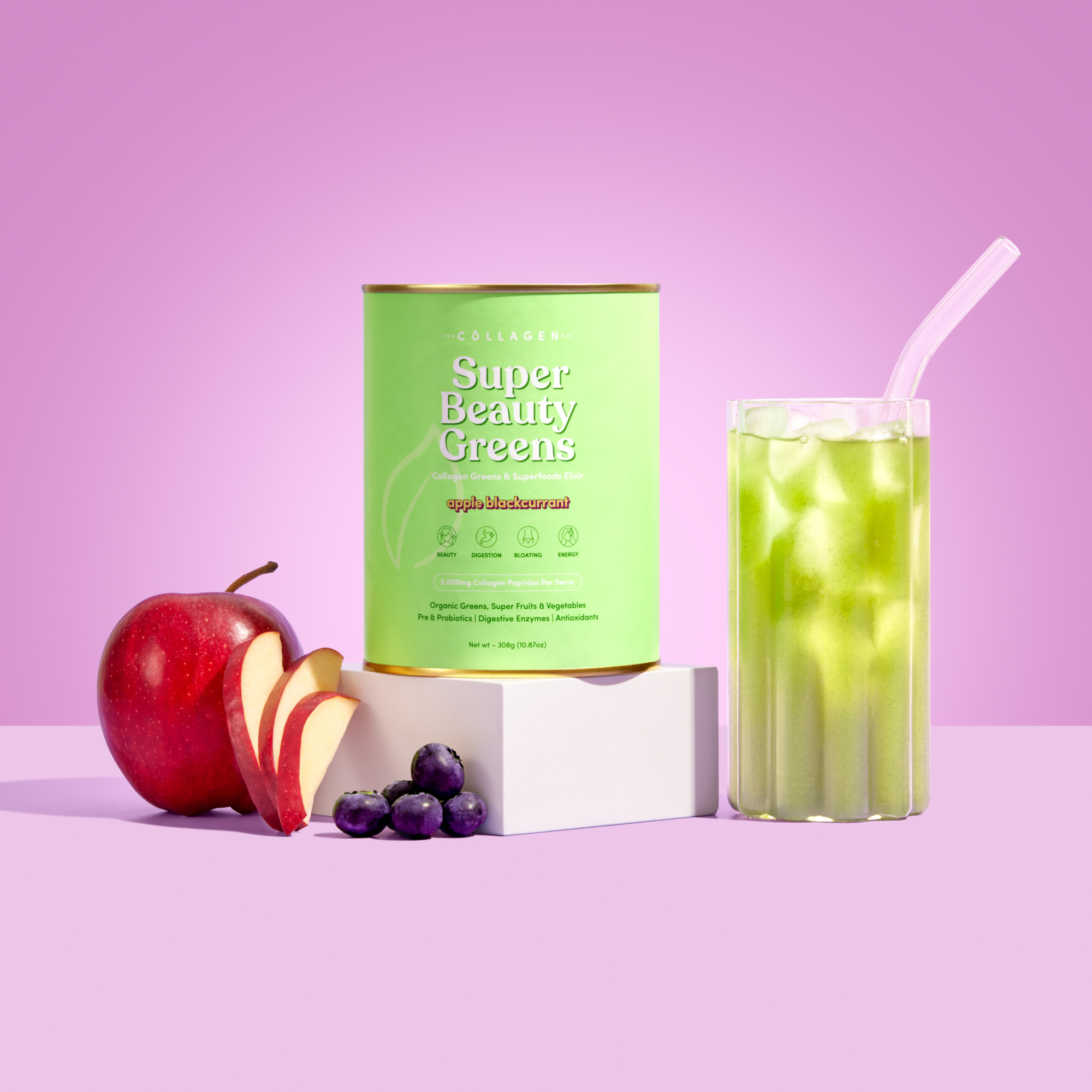 Green collagen supplement container with apple slices, berries, and a green drink with a straw on a pink background.