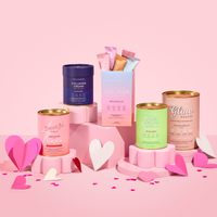 The Collagen Co. The Complete Glow Affair Bundle, featuring vibrant wellness powders and stick packs for gut health and wellness, is displayed on pink platforms with paper hearts against a lively pink background.