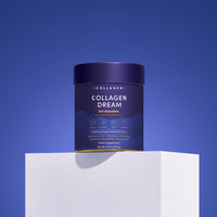 A container of The Collagen Co. Collagen Dream Advanced Sleep Formula Hot Chocolate (210g) sits on a white pedestal against a blue gradient background, showcasing its dark blue, gold, and white packaging for relaxation and skin health.