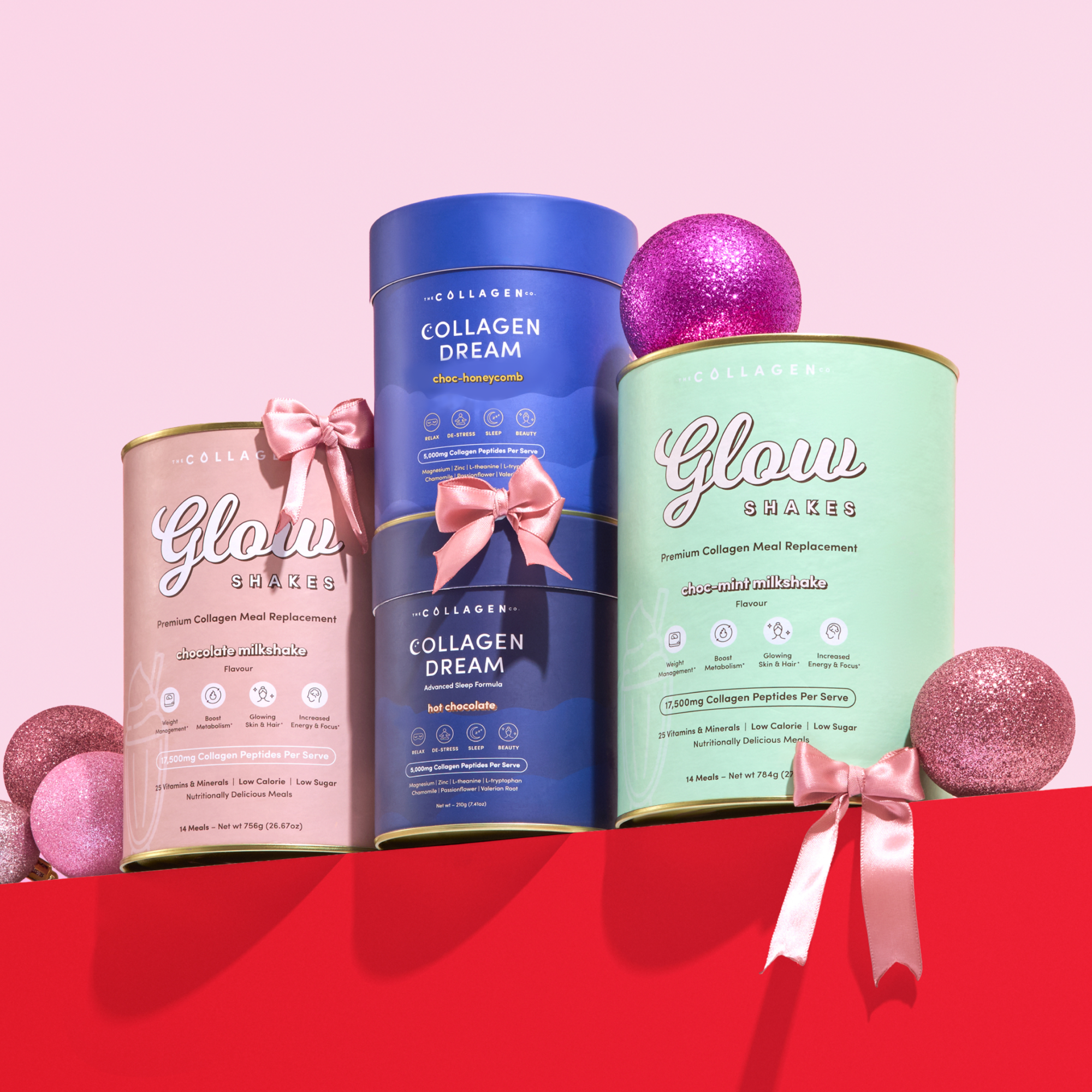 The Collagen Co. Festive Treats Wellness Kit features pastel canisters of Glow Shakes collagen meal replacements with pink satin bows, displayed among glittery ornaments on a vibrant pink background—ideal for your wellness routine.