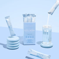 A box of thecollagen.co Unflavored Collagen Sachets (210g) rests on a blue surface with individual packets nearby. One sachet is being mixed into a glass of water, promoting healthy hair, skin, and nails in a light blue and white setting.