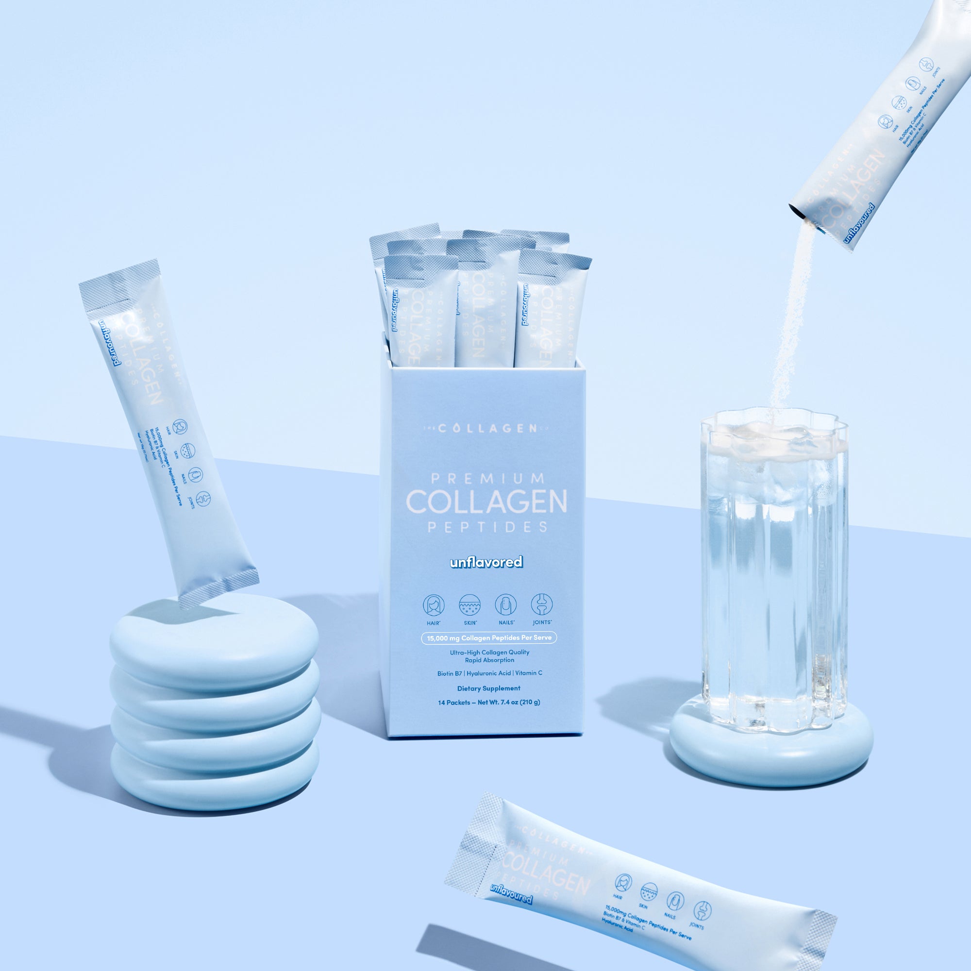 A box of thecollagen.co Unflavored Collagen Sachets (210g) rests on a blue surface with individual packets nearby. One sachet is being mixed into a glass of water, promoting healthy hair, skin, and nails in a light blue and white setting.