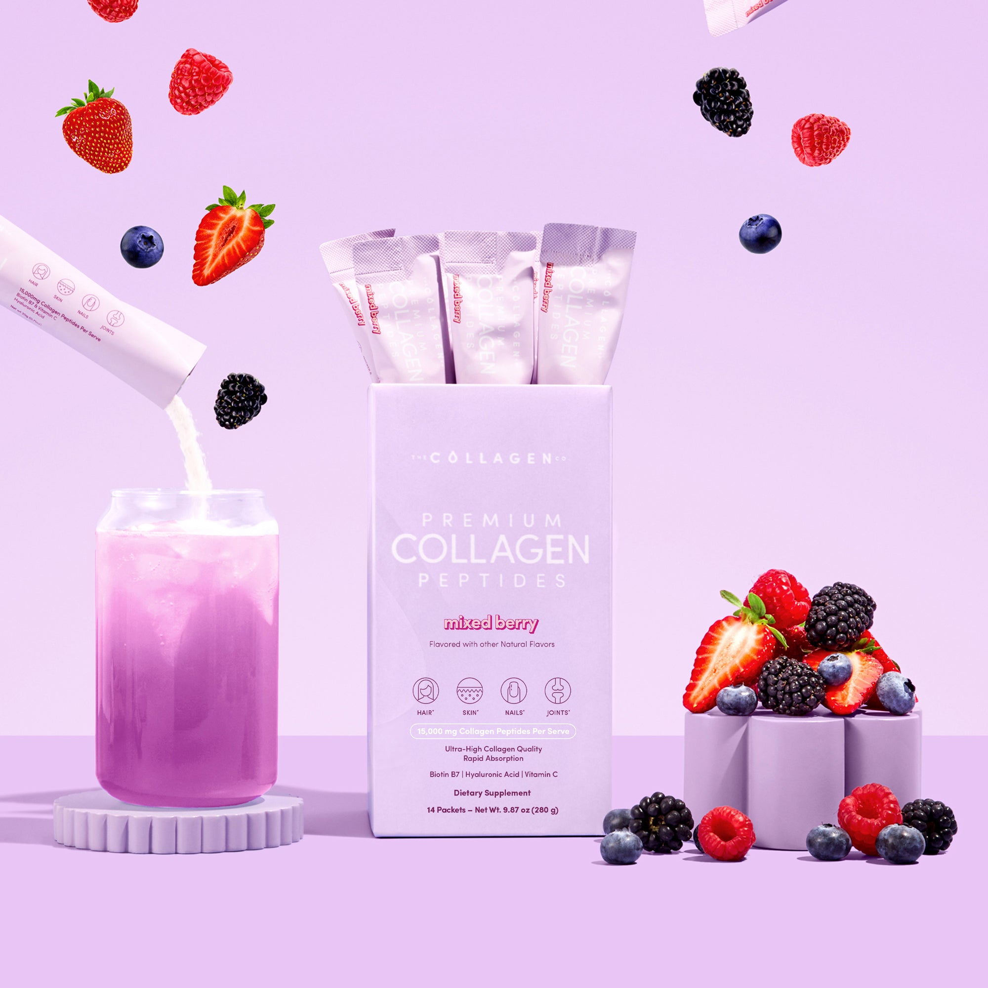 A jar of pink drink from The Collagen Co. Mixed Berry Collagen Sachets - 280g is poured beside its box, surrounded by fresh mixed berries on a pastel purple background.
