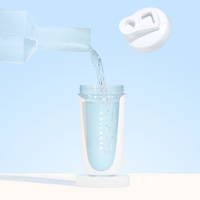 A close-up of water poured from a glass pitcher into The Collagen Co. White Collagen Protein Shaker - 600ml, labeled “Collagen,” with its BPA-free white lid open and floating above against a light blue background—a perfect fitness companion.