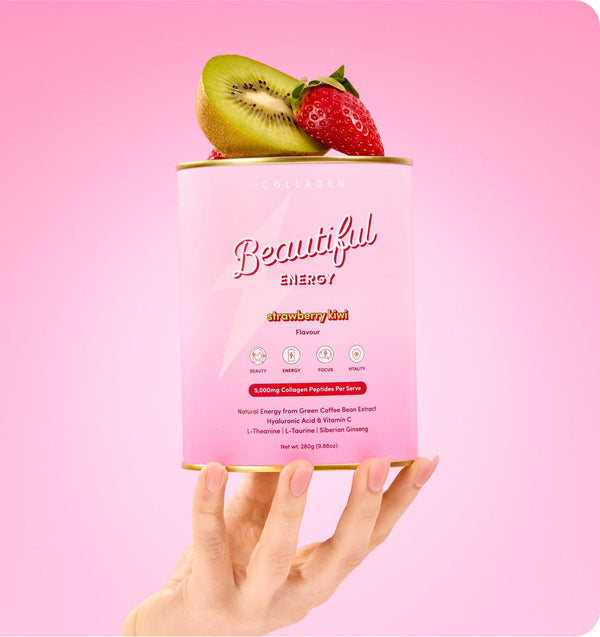 A hand holds a pink container of Beautiful Energy strawberry kiwi collagen powder against a pink background, topped with a sliced kiwi and a strawberry.