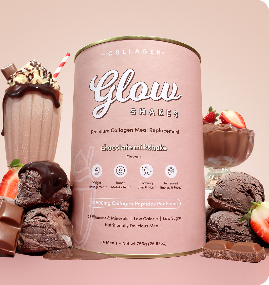 A tub of Glow Shakes chocolate milkshake meal replacement sits surrounded by chocolate ice cream, milkshake glasses with whipped cream, chocolate bars, and strawberries against a light pink background.