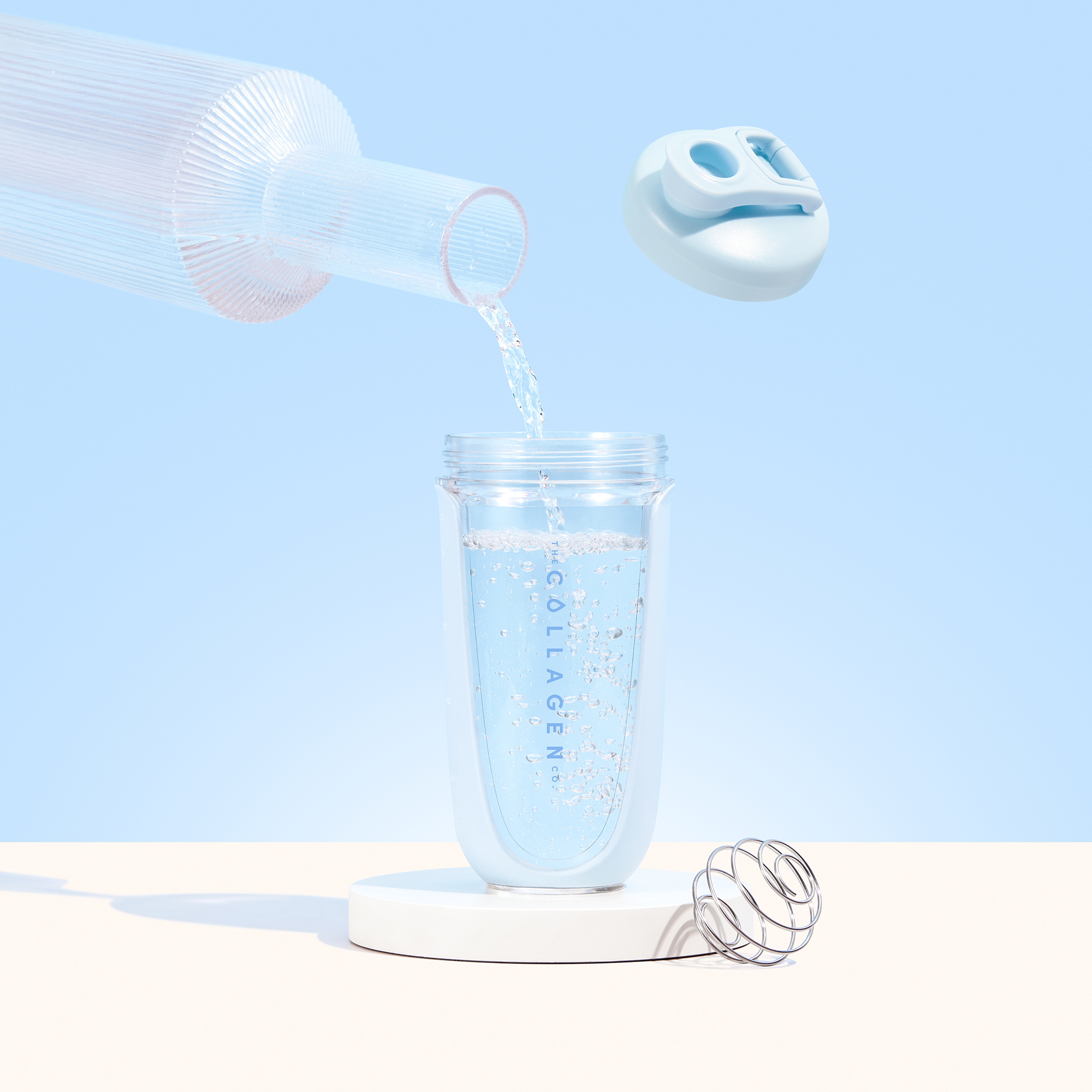 Pouring water into a clear collagen container with a whisk and detachable lid against a pastel blue background.